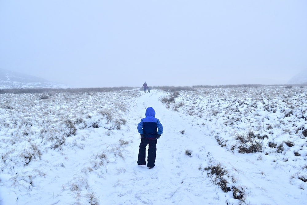 person in blue jacket walking on snow covered field during daytime