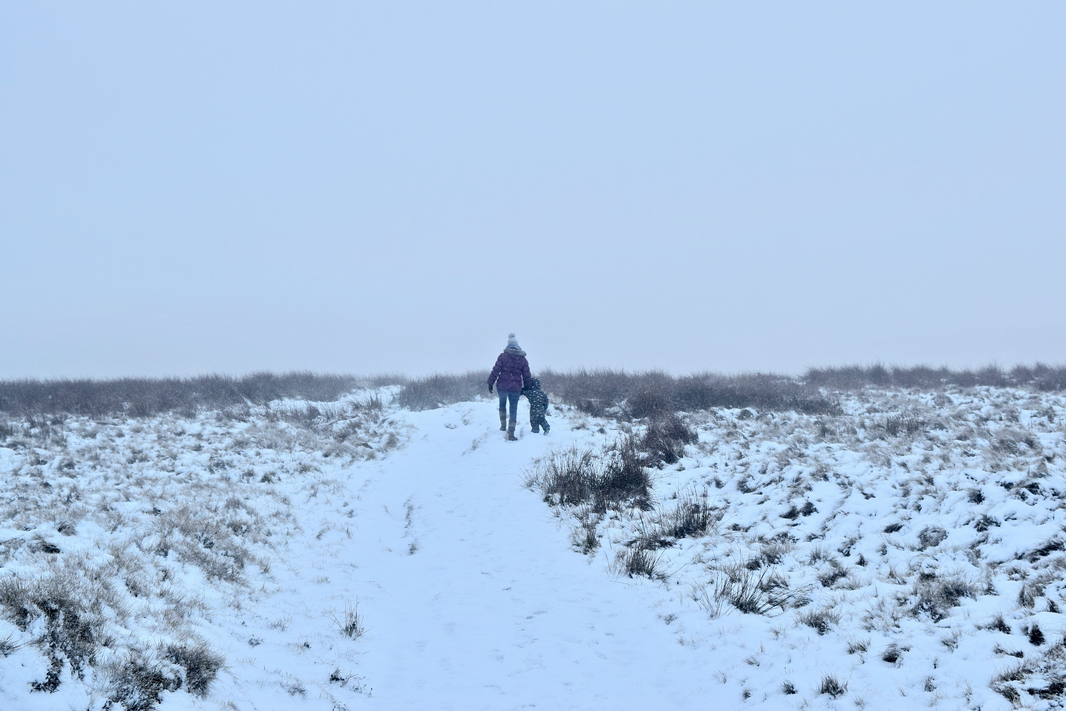 person in black jacket walking on snow covered field during daytime