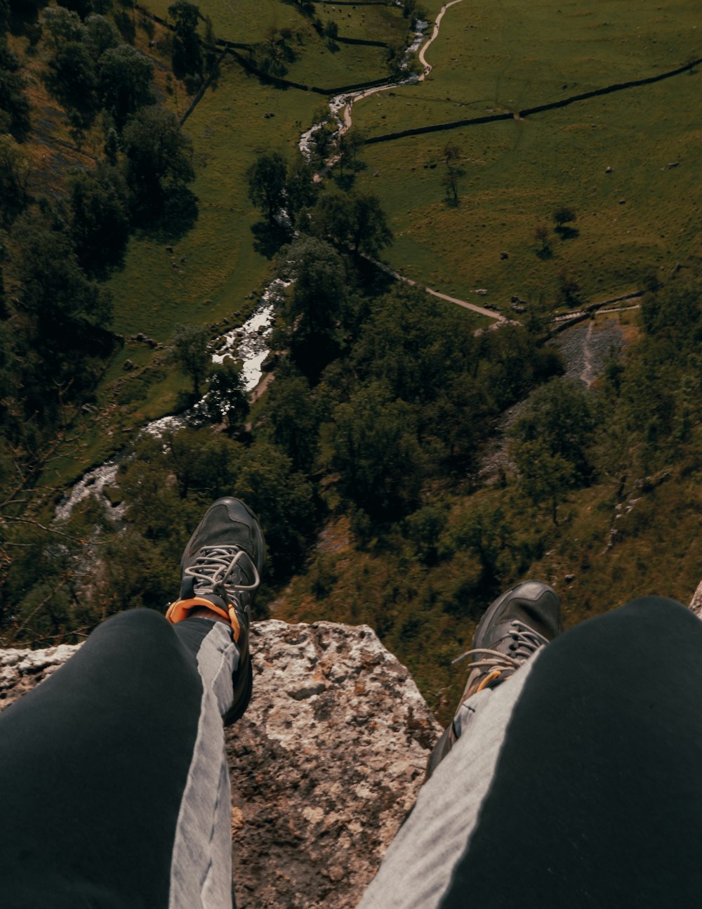 person in black pants and gray hiking shoes sitting on rock mountain during daytime