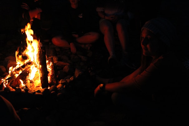 A vibrant group of travelers laughing around a campfire at sunset in the mountains.