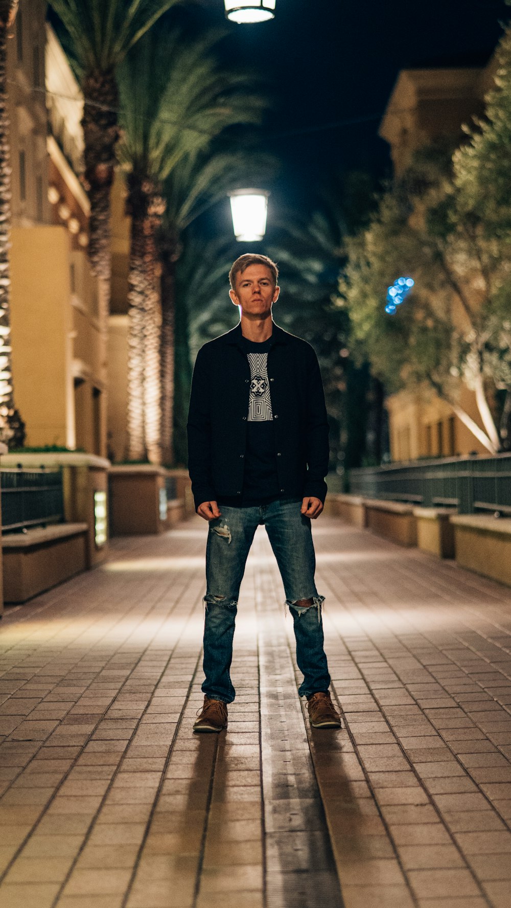 man in black sweater standing on sidewalk during night time