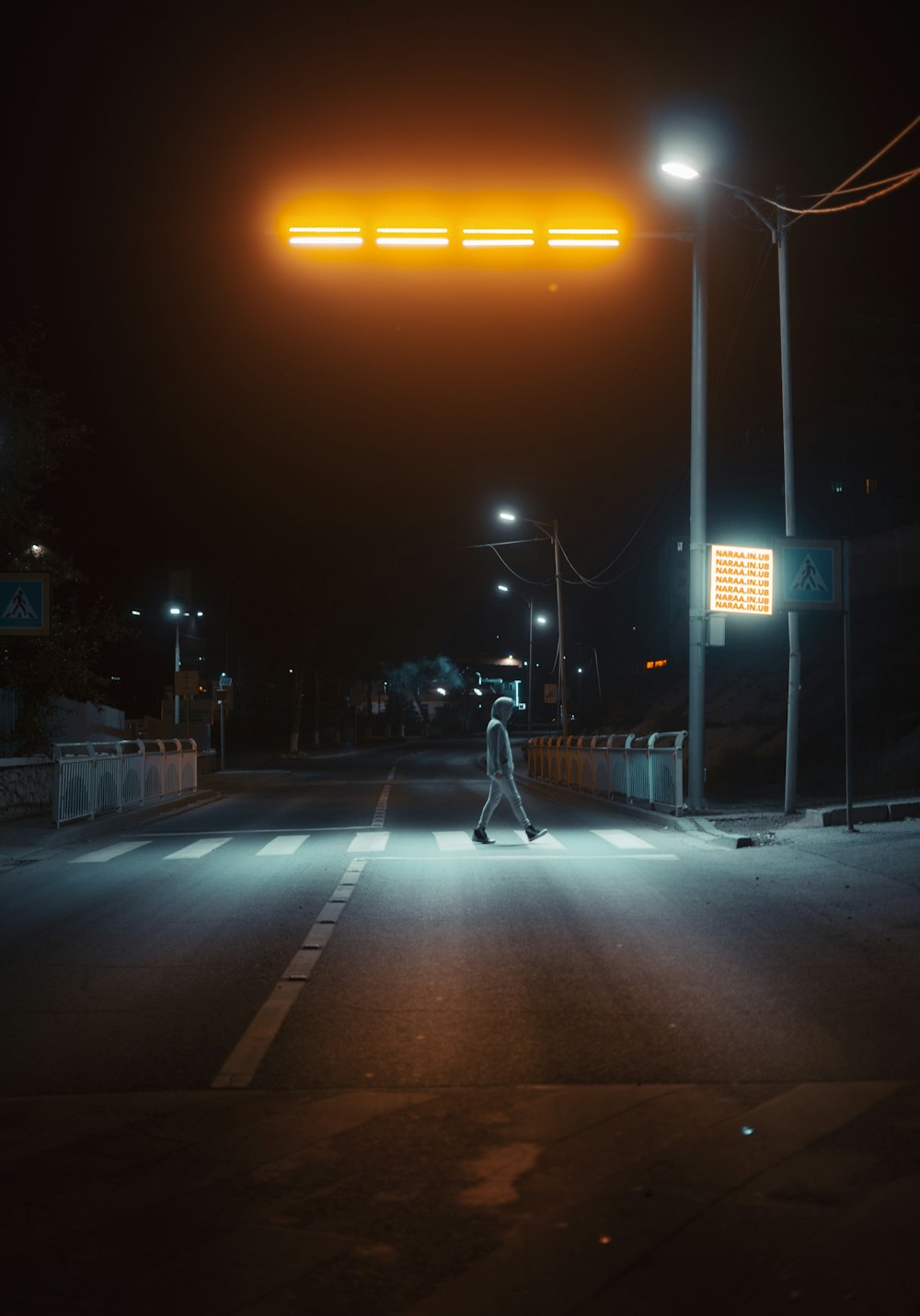 man in black jacket and blue denim jeans walking on sidewalk during night time