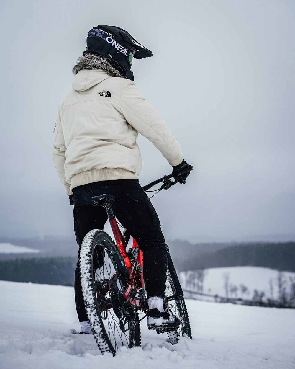 person in beige jacket riding black and red mountain bike on snow covered ground during daytime