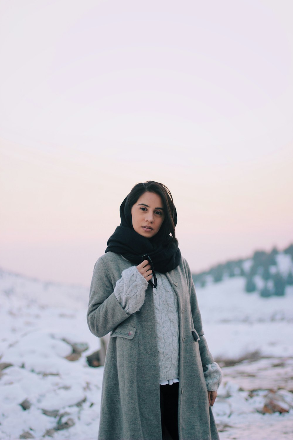 woman in gray coat standing on snow covered ground during daytime