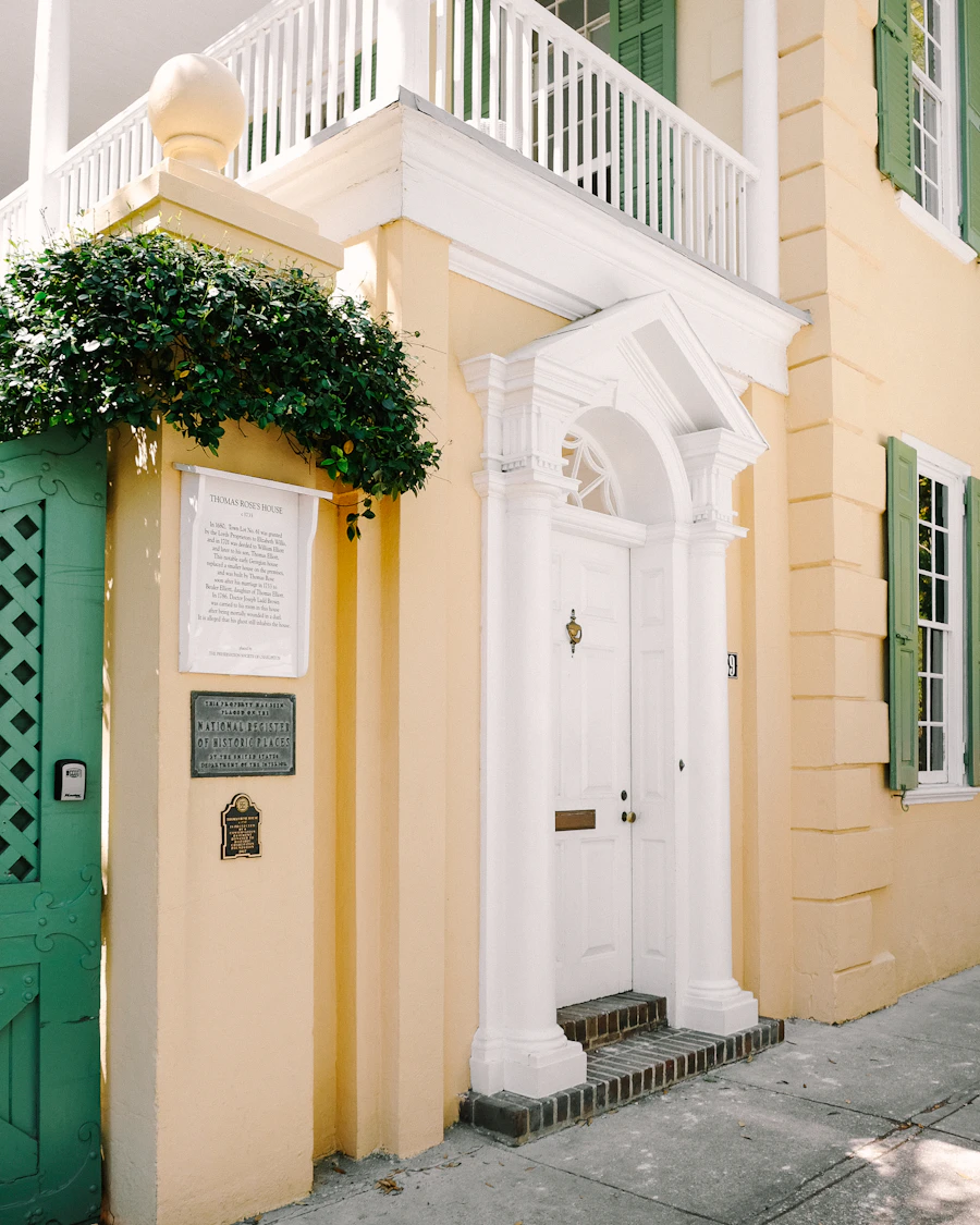 A yellow house with a white columned doorway and green gate