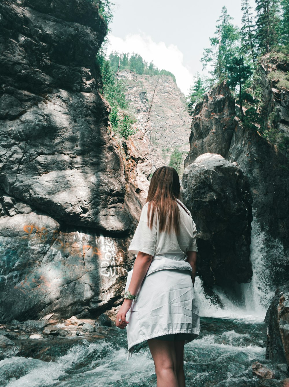 Frau in weißem Hemd und weißem Rock, die tagsüber in der Nähe von Wasserfällen steht