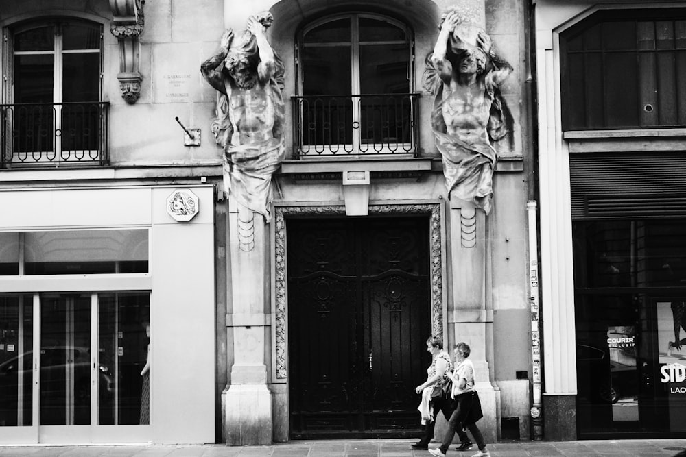 grayscale photo of man and woman standing in front of building