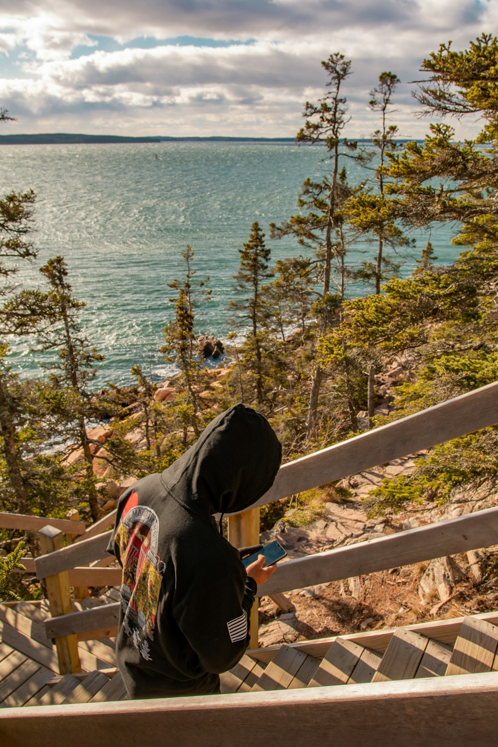 person in black hoodie sitting on brown wooden bench near body of water during daytime