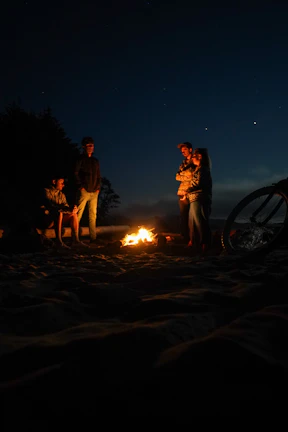 A cozy campfire scene on a beach at dusk, with friends sharing stories under a starry sky.