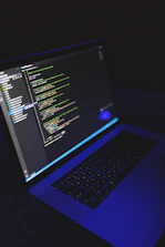 A developer coding on a laptop with futuristic blue and dark tones in the background.