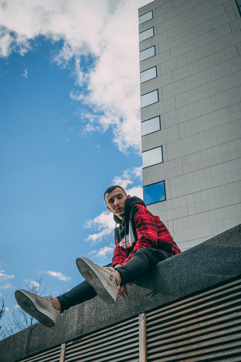 woman in red and black jacket sitting on gray concrete wall during daytime