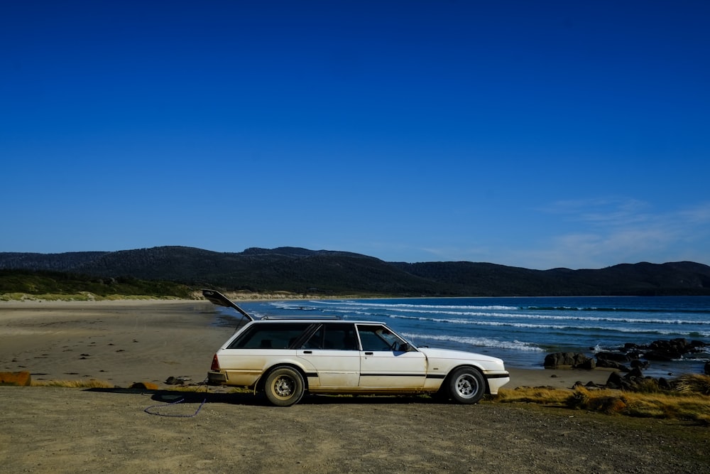 white station wagon on brown sand near body of water during daytime
