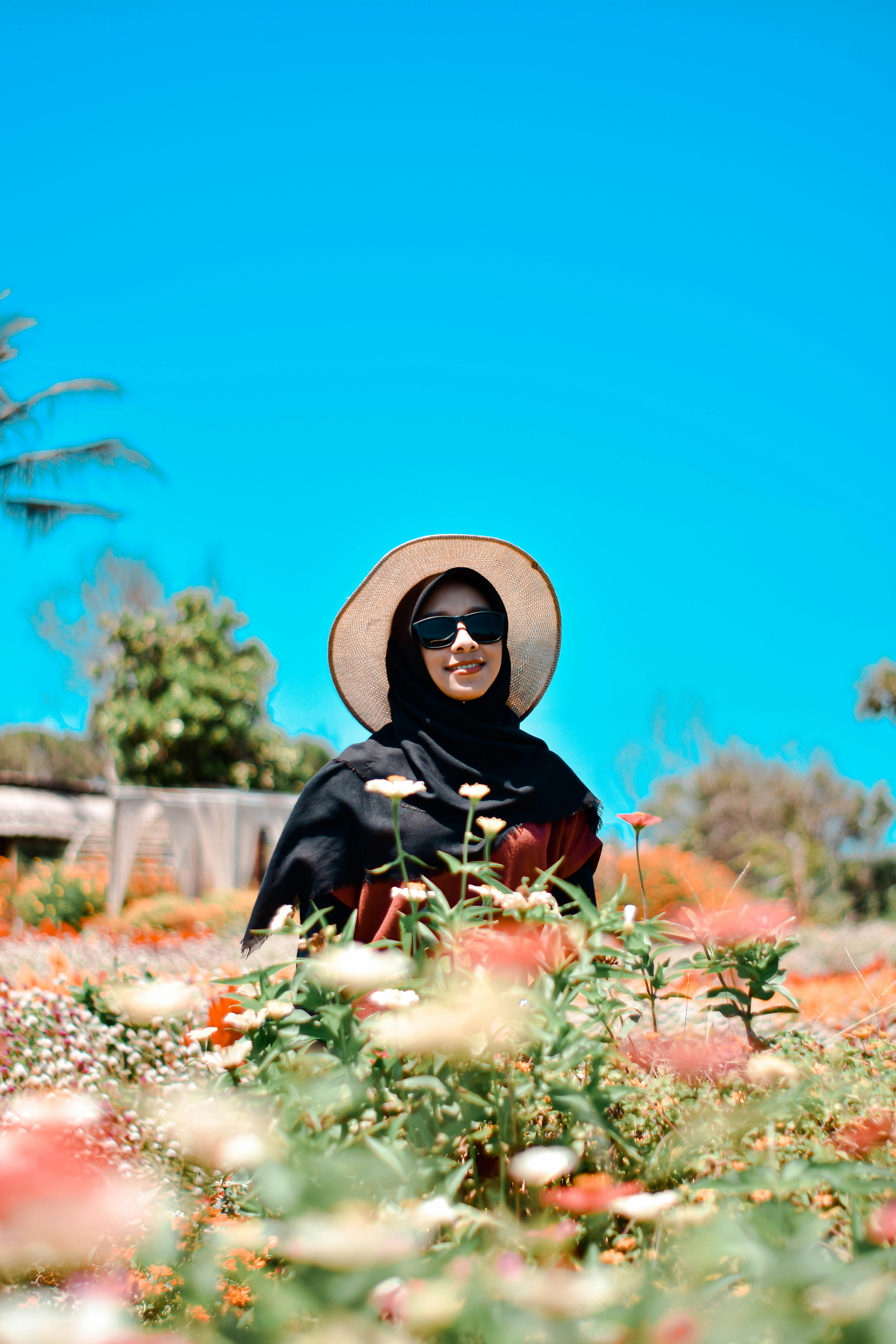 wanita berjilbab hitam dan putih duduk di atas daun kering coklat di siang hari