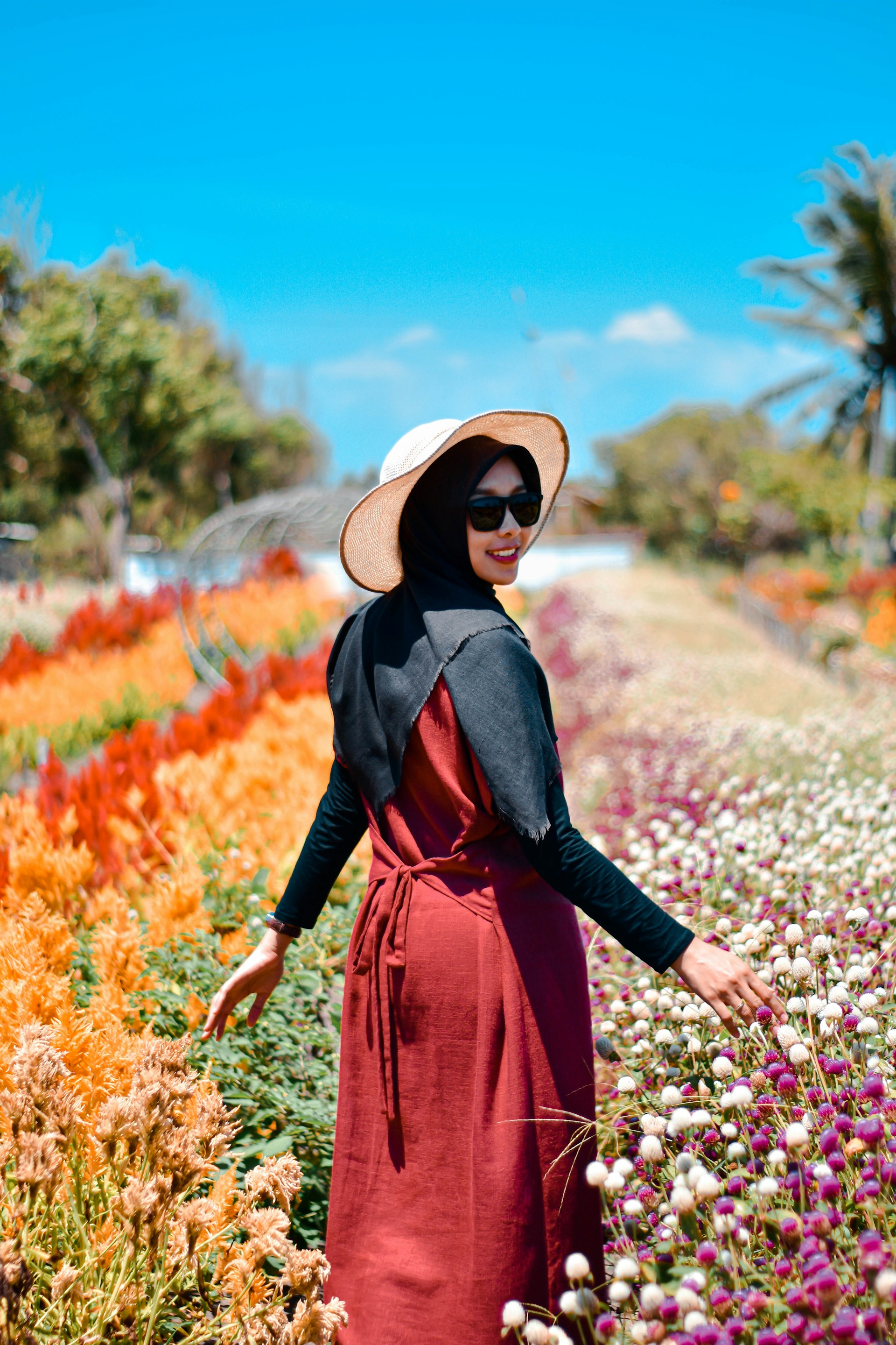 woman in black leather jacket and brown sun hat standing on flower field during daytime