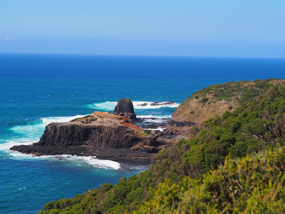 brown and green mountain beside blue sea under blue sky during daytime