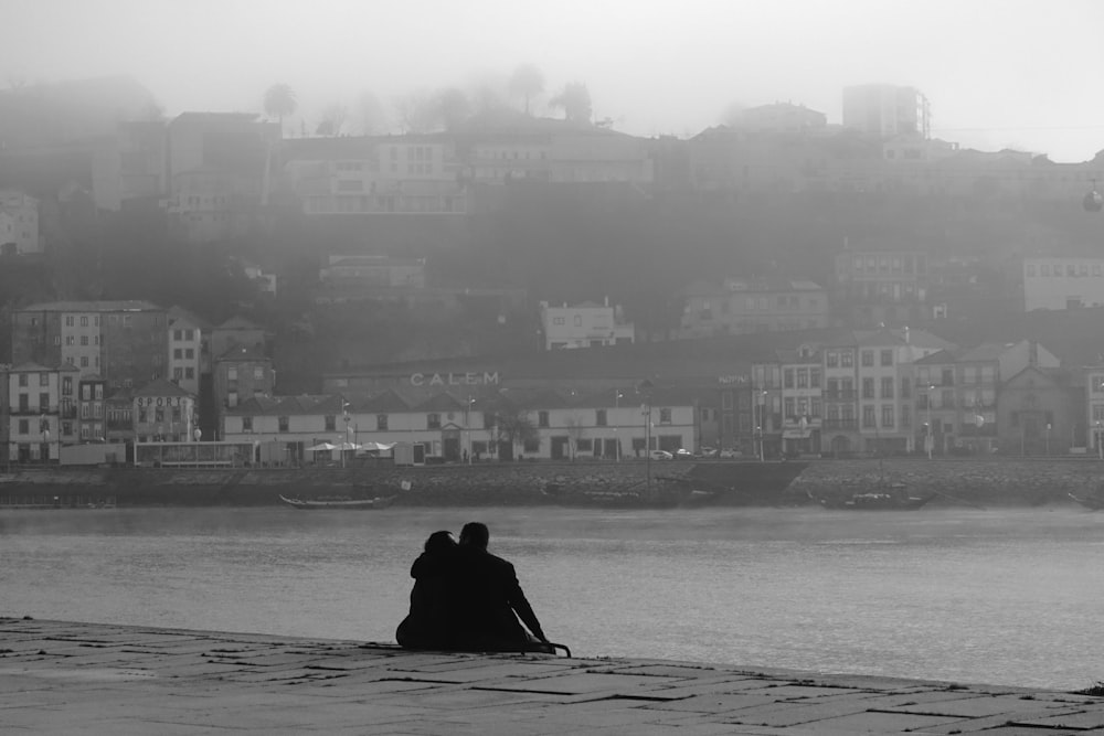 silhouette of person sitting on rock near body of water during daytime