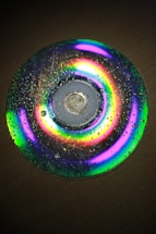 A compact disc with water droplets on its surface, displaying a spectrum of vibrant colors due to light diffraction.