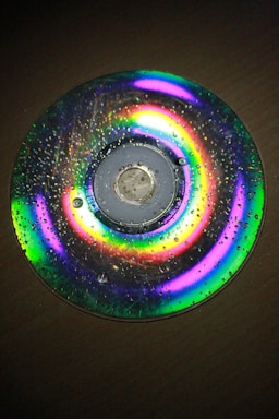 A compact disc with water droplets on its surface, displaying a spectrum of vibrant colors due to light diffraction.
