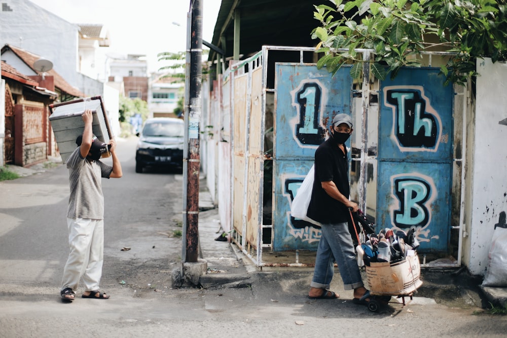 man in black t-shirt and white pants standing beside blue wooden door during daytime