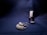A bottle of deep red nail polish stands upright on a dark, textured fabric surface. Beside it, a delicate pair of earrings adorned with small, light-colored pearls rests on the same surface, casting soft shadows.