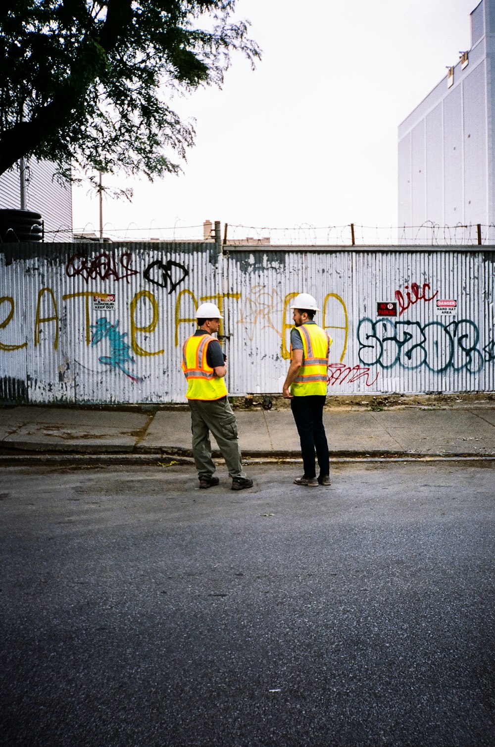 Mann in gelber Jacke und schwarzer Hose steht tagsüber mit Graffiti an der Wand