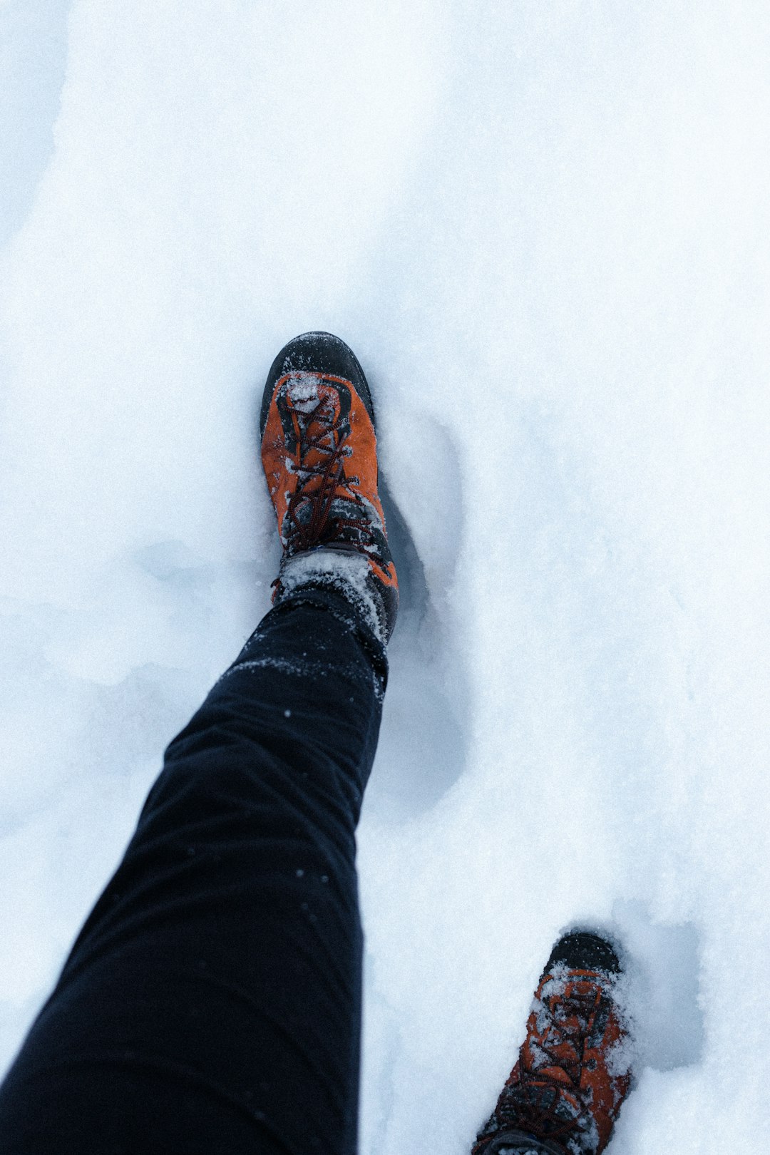 person in black pants and brown hiking shoes standing on snow covered ground