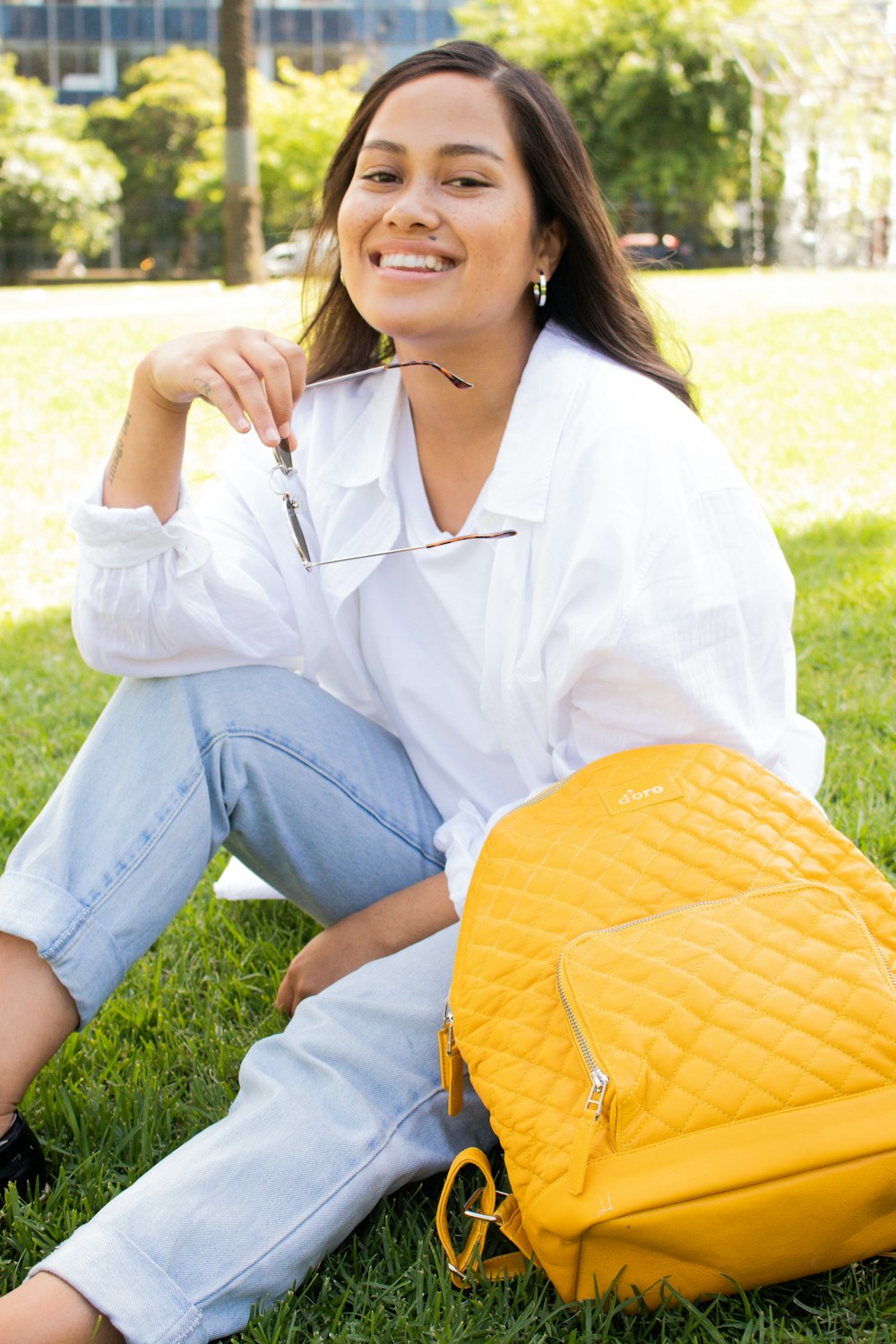 하얀 드레스 셔츠와 푸른 데님 청바지를 입은 여자가 낮 동안 푸른 잔디밭��에 앉아 있다