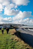 A scenic coastal path with travelers walking along the cliffs under a bright sky.