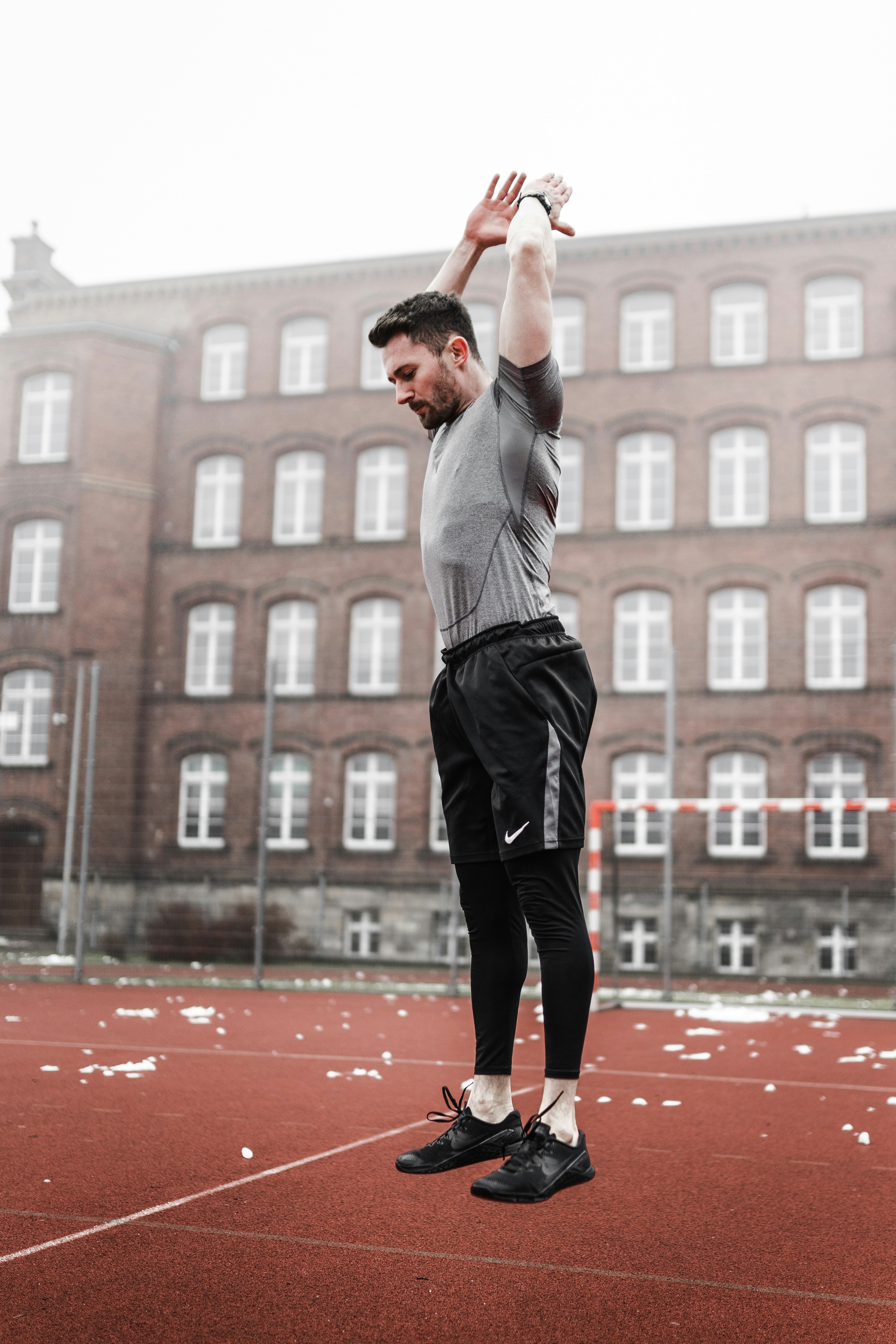 Mann in grauem Langarmhemd und schwarzer Hose, der tagsüber auf rotem Betonboden steht