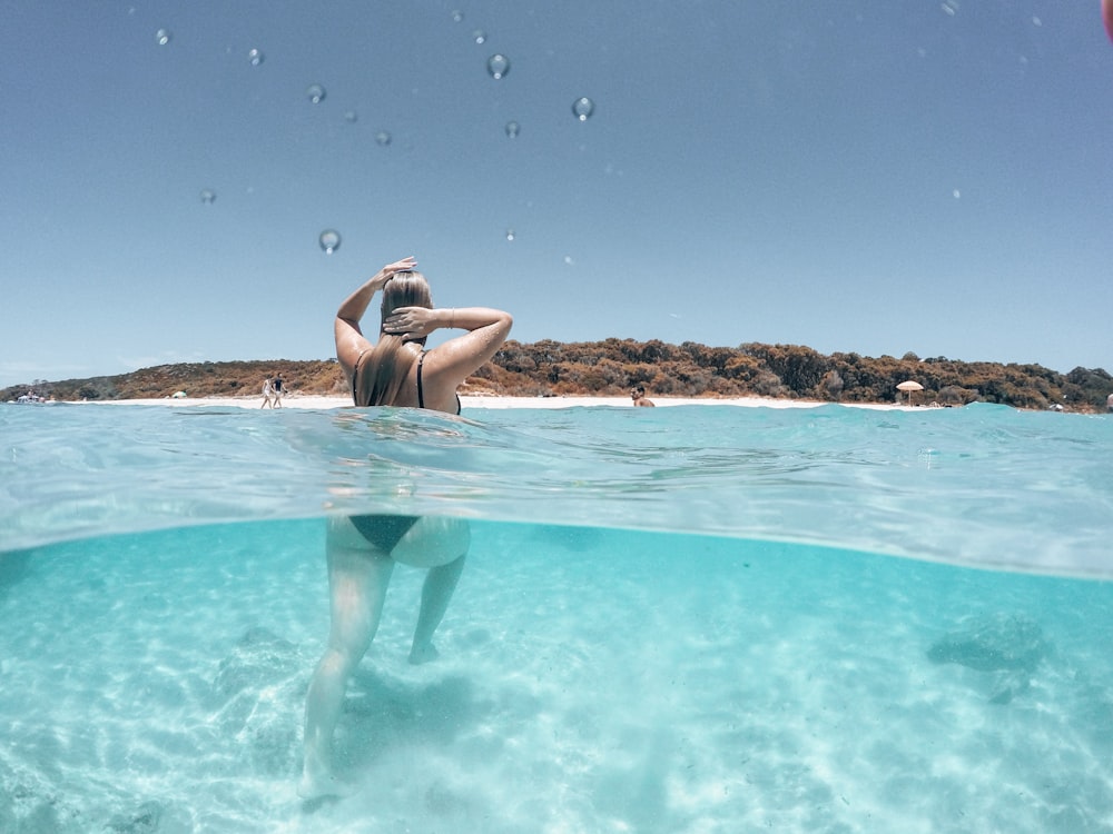 woman in black bikini lying on body of water during daytime