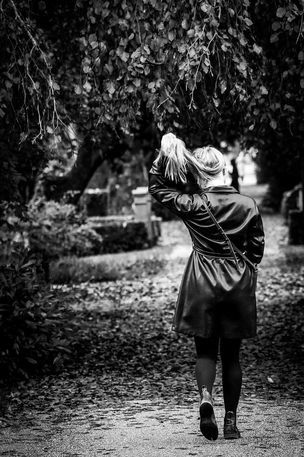 grayscale photo of woman in black coat standing on road