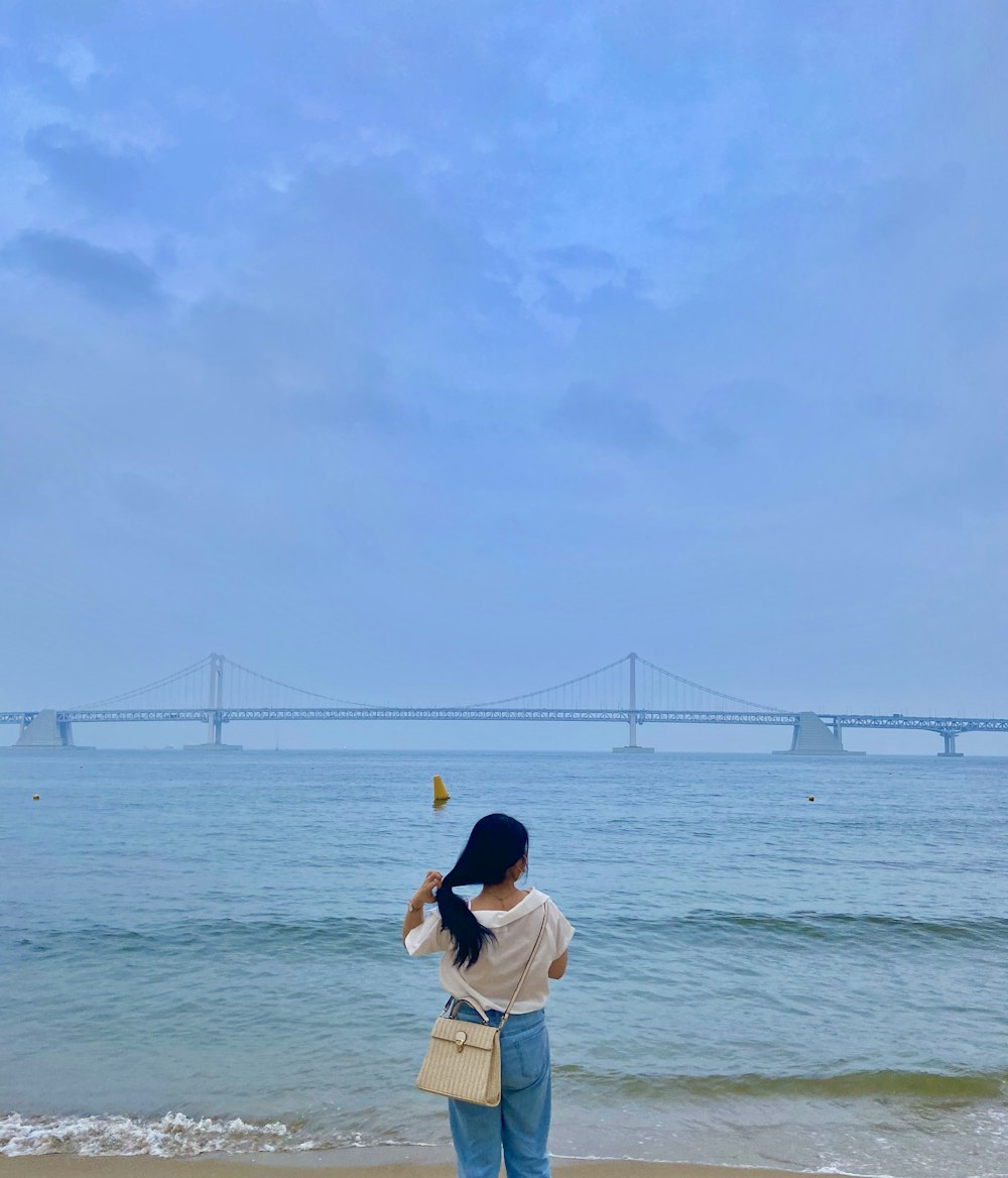 흰색 셔츠와 파란색 데님 반바지를 입은 여자가 낮 동안 바닷가에 서 있다