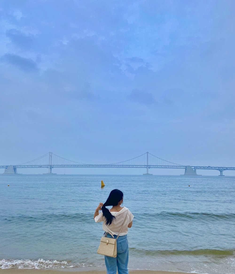 woman in white shirt and blue denim shorts standing on sea shore during daytime