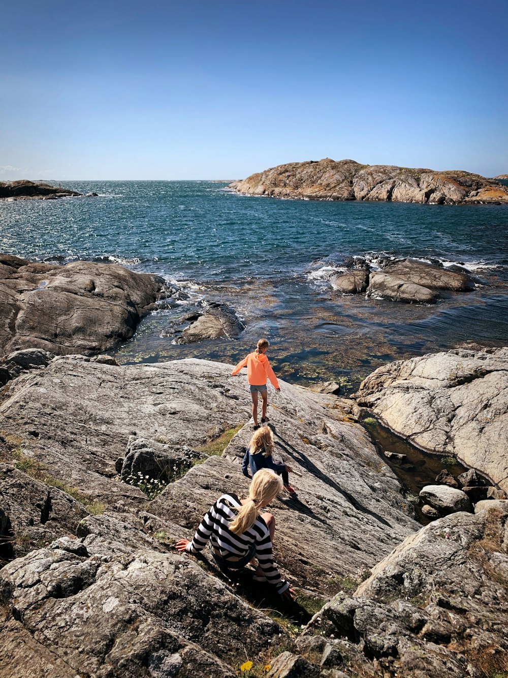 femme en débardeur orange et pantalon noir et blanc debout sur le rivage rocheux pendant la journée
