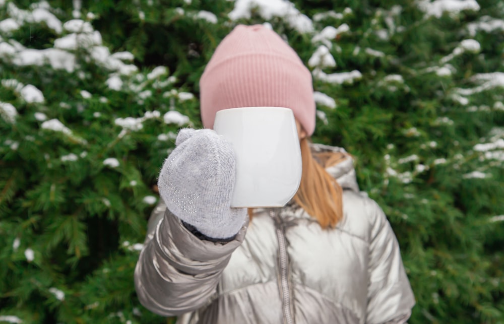 woman in gray jacket and red knit cap covering face with white paper