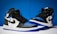 A pair of high-top athletic sneakers with a predominantly black, blue, and white color scheme is placed on a contrasting background. The shoes feature black laces and a distinctive logo on the side.