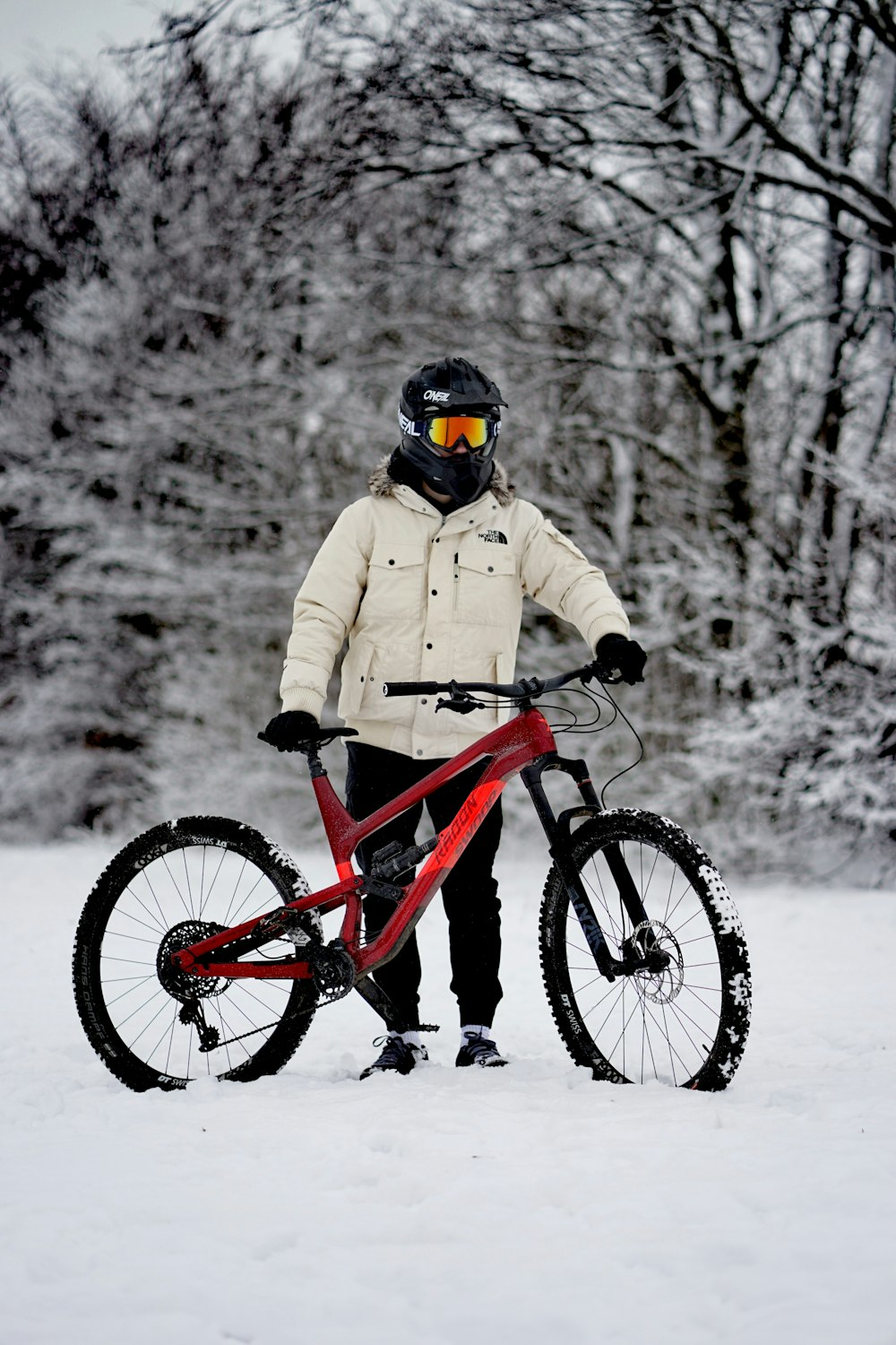 pessoa em jaqueta marrom que monta mountain bike vermelha no chão coberto de neve durante o dia