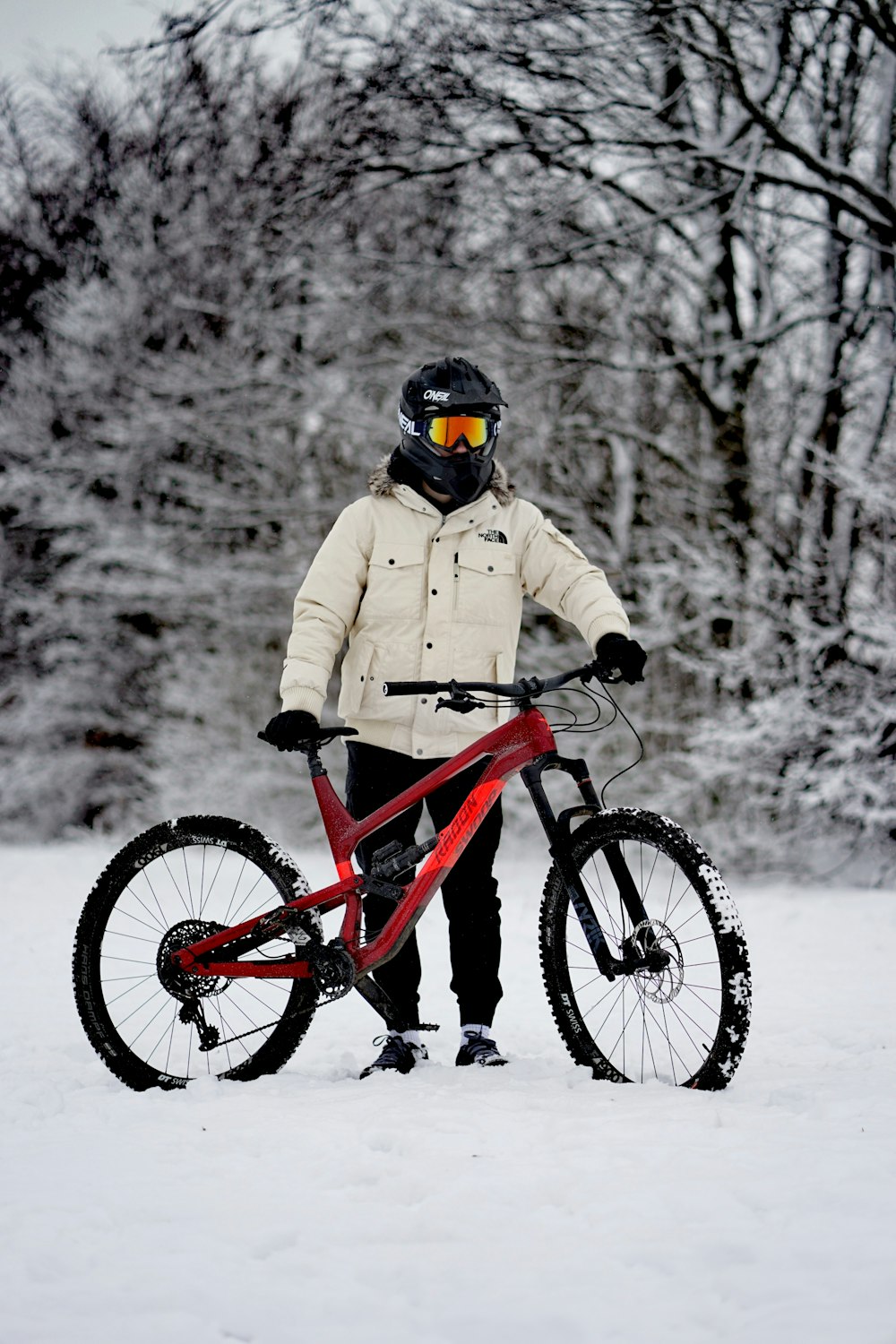 person in brown jacket riding red mountain bike on snow covered ground during daytime
