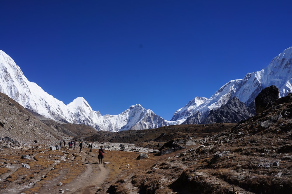 people walking on dirt road near snow covered mountains during daytime