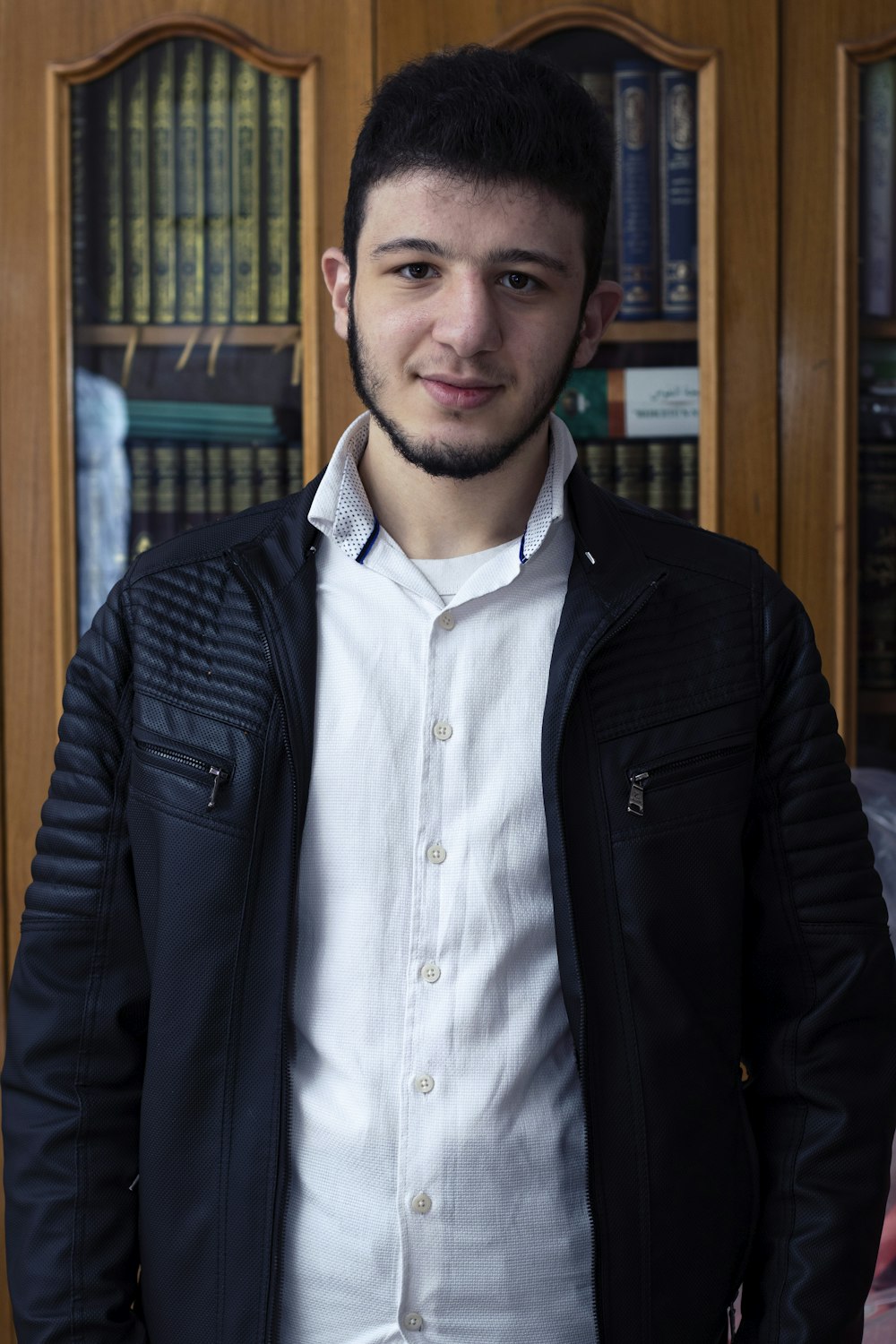 man in black jacket standing near brown wooden shelf