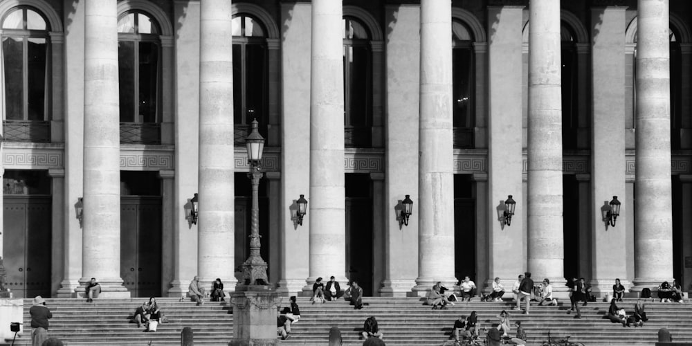 grayscale photo of people sitting on bench in front of building