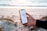 A person holds a smartphone displaying a speed test result while standing on a sandy beach. The ocean is in the background with gentle waves and a serene atmosphere. The phone's screen shows a speed of 184.56 Mbps and is held firmly by a hand wearing a dark sleeve.
