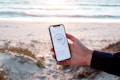 A person holds a smartphone displaying a speed test result while standing on a sandy beach. The ocean is in the background with gentle waves and a serene atmosphere. The phone's screen shows a speed of 184.56 Mbps and is held firmly by a hand wearing a dark sleeve.