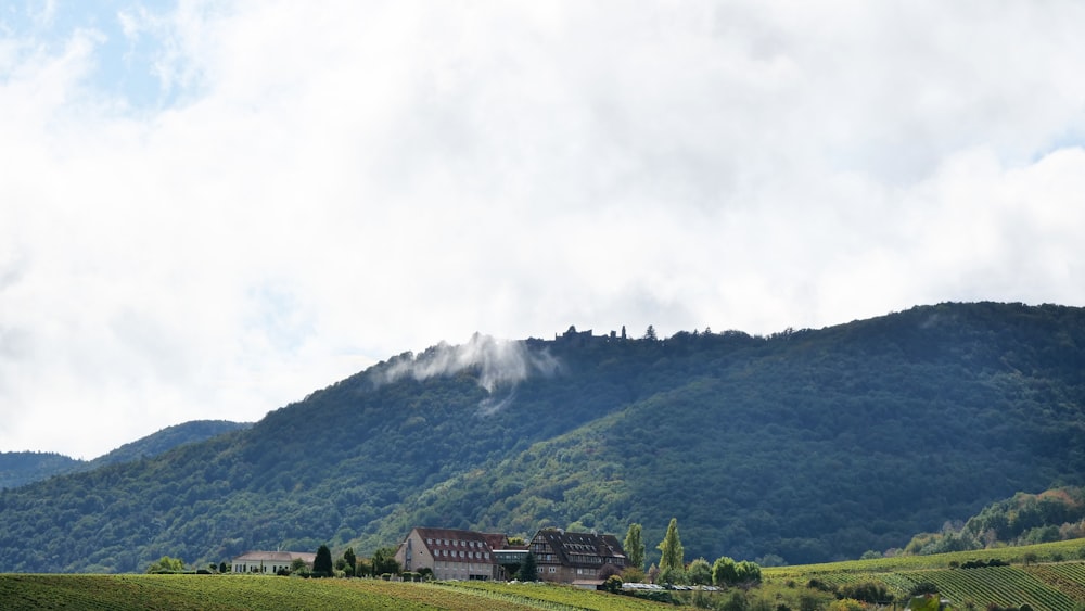 green grass field near mountain under white clouds during daytime