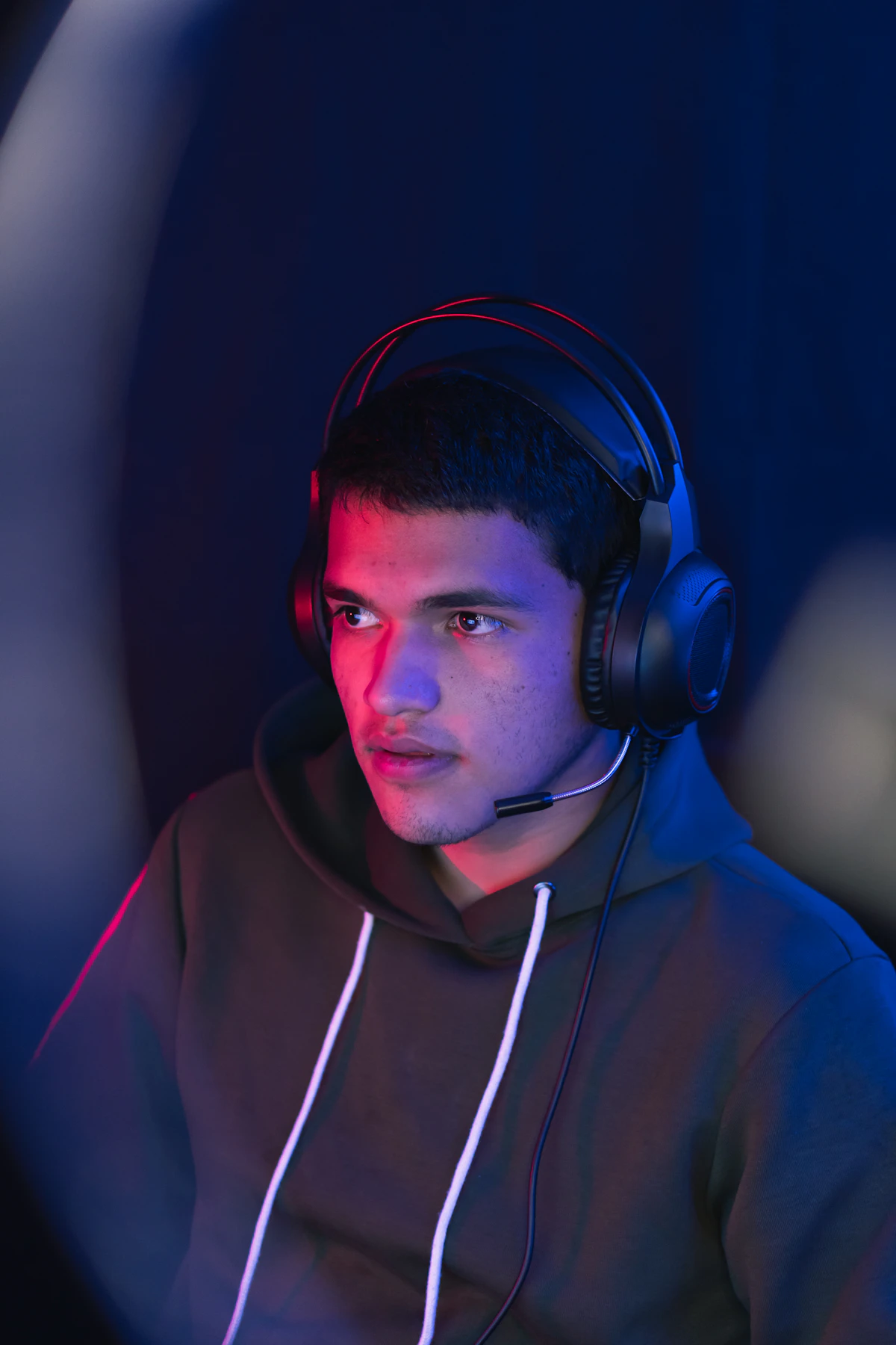 Person in a hoodie wearing headphones, lit by red and blue light