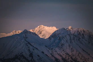 Snow-capped peaks glowing softly at sunrise above a quiet valley.