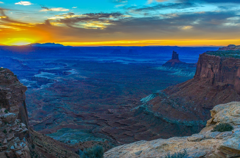 person sitting on rock formation near body of water during sunset