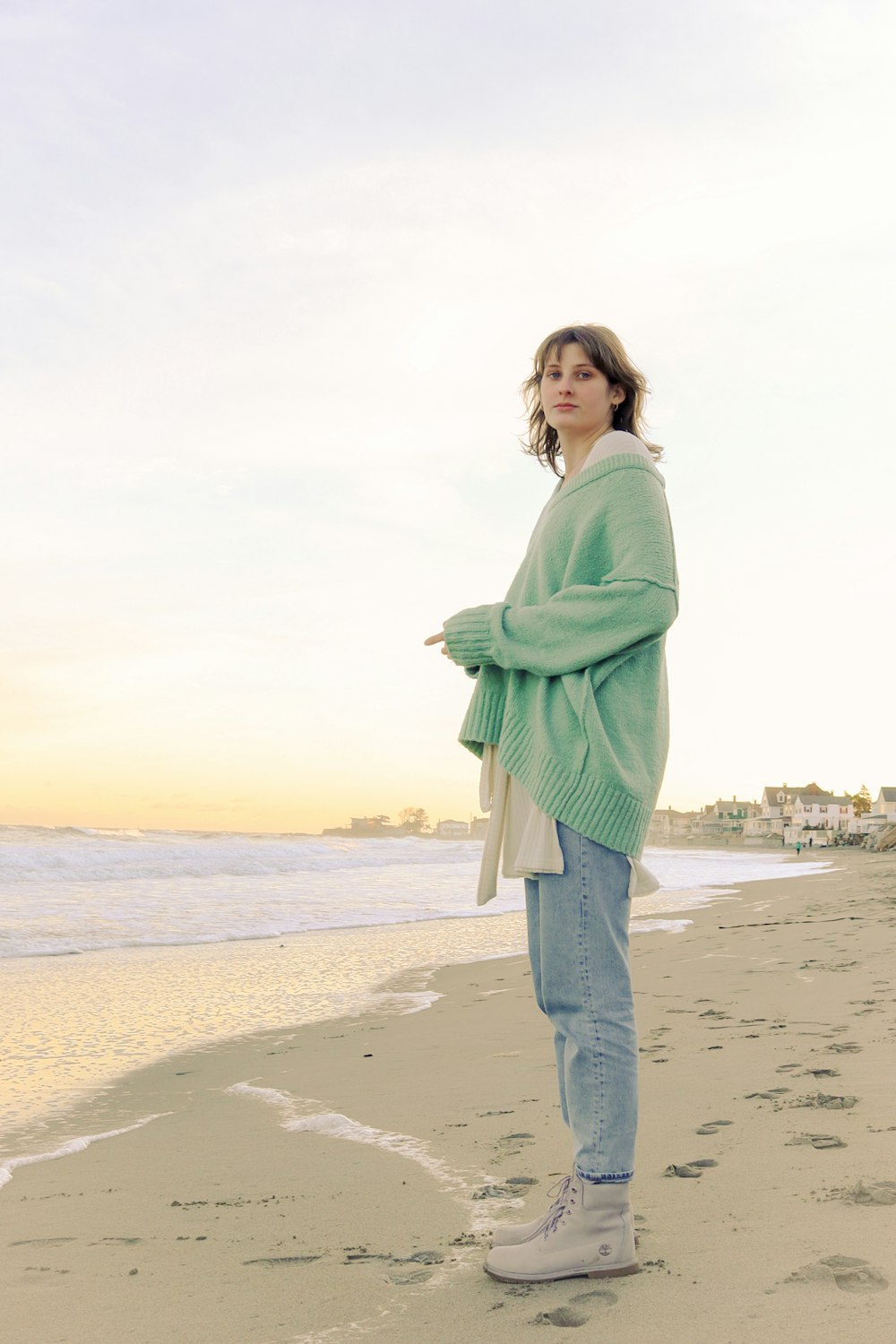 woman in green long sleeve shirt and blue denim jeans standing on beach during daytime