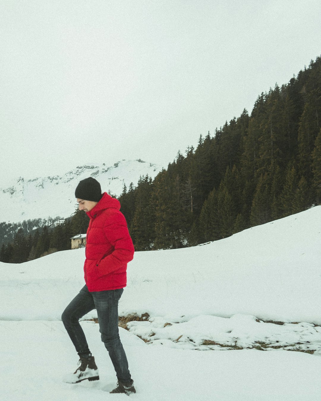 man in red jacket and black pants standing on snow covered ground during daytime