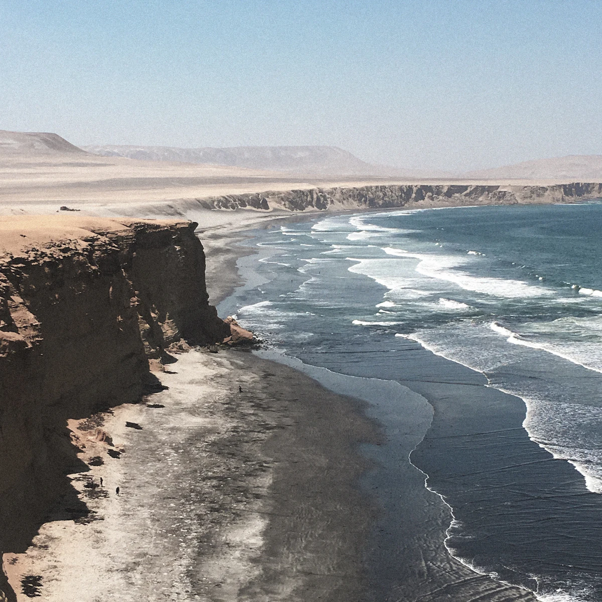 Dark cliffs above a long beach on the Paracas coast, with pale desert hills behind